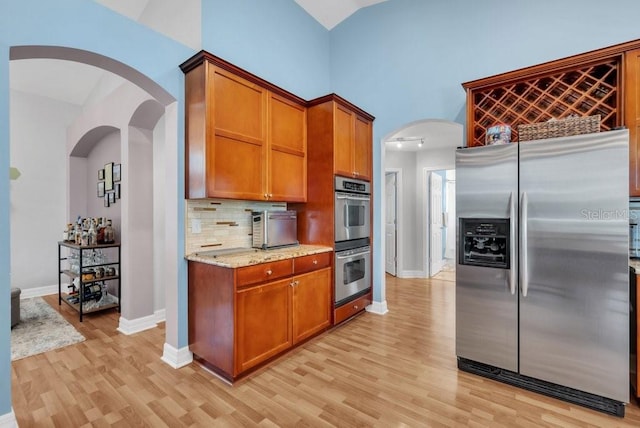 15309 Palomapark Ln, Lithia, FL 33547 - kitchen featuring appliances with stainless steel finishes, light wood-type flooring, decorative backsplash, light stone countertops, and high vaulted ceiling