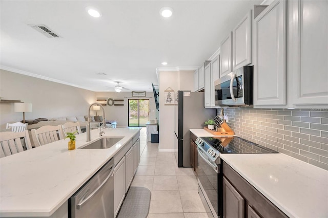 14716 Crescent Rock Dr, Wimauma, FL 33598 - kitchen with stainless steel appliances, a sink, ceiling fan, decorative backsplash, and an island with sink