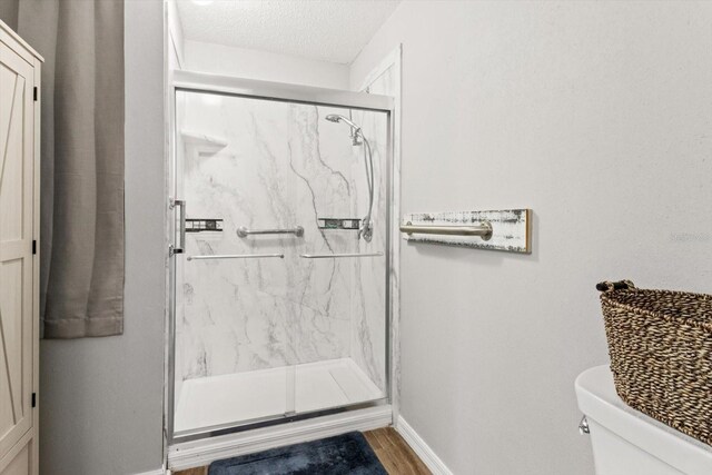 2541 W Castle Rd, Citrus Springs, FL 34434 - bathroom with a marble finish shower, toilet, baseboards, a textured ceiling, and wood finished floors