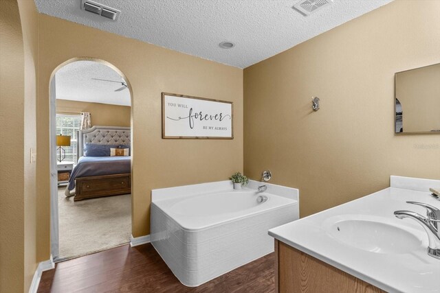 2541 W Castle Rd, Citrus Springs, FL 34434 - ensuite bathroom featuring a textured ceiling, a garden tub, wood finished floors, vanity, and baseboards
