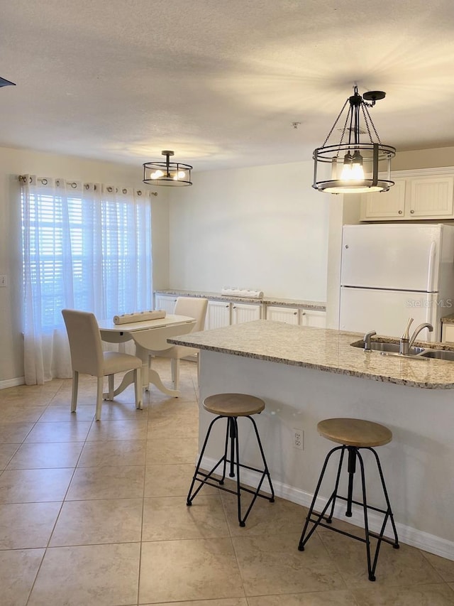 850 S Tamiami Trl Unit 424, Sarasota, FL 34236 - kitchen with freestanding refrigerator, a sink, a kitchen bar, hanging light fixtures, and light stone counters