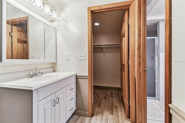 12101 Meadowbrook Ln, Hudson, FL 34667 - bathroom featuring wood finished floors, vanity, a walk in closet, a stall shower, and a textured ceiling