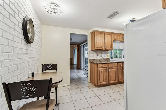 12101 Meadowbrook Ln, Hudson, FL 34667 - kitchen with freestanding refrigerator, light tile patterned floors, brown cabinets, stone countertops, and tasteful backsplash