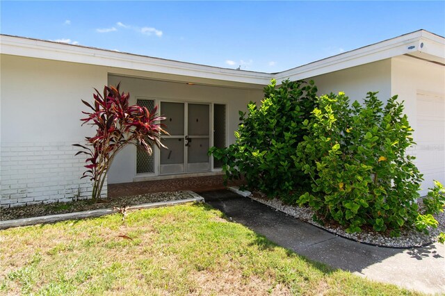 13898 Jamaica Dr, Seminole, FL 33776 - entrance to property with stucco siding, brick siding, a garage, and a lawn
