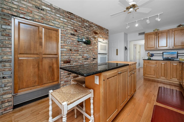 224 Harbor View Ln, Largo, FL 33770 - kitchen featuring double oven, light wood-type flooring, a kitchen island, brick wall, and a ceiling fan
