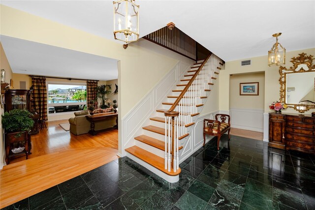 224 Harbor View Ln, Largo, FL 33770 - stairs featuring a chandelier, granite floors, and a wainscoted wall