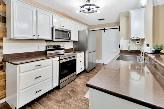 9615 Raiden Ln, Riverview, FL 33569 - kitchen featuring stainless steel appliances, dark countertops, a sink, a barn door, and white cabinetry