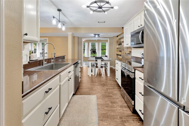 9615 Raiden Ln, Riverview, FL 33569 - kitchen with stainless steel appliances, a sink, decorative columns, white cabinets, and tasteful backsplash