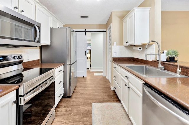9615 Raiden Ln, Riverview, FL 33569 - kitchen with stainless steel appliances, a sink, white cabinets, a barn door, and light wood finished floors