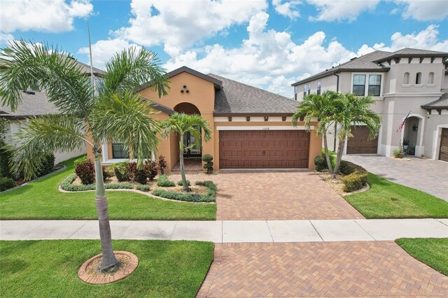 13128 Foxtail Fern Dr, Riverview, FL 33579 - mediterranean / spanish-style home with stucco siding, decorative driveway, a front lawn, an attached garage, and a shingled roof