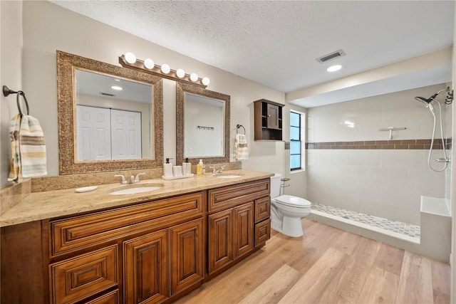 4509 Grainary Ave, Tampa, FL 33624 - full bathroom featuring double vanity, tiled shower, toilet, wood finished floors, and a textured ceiling