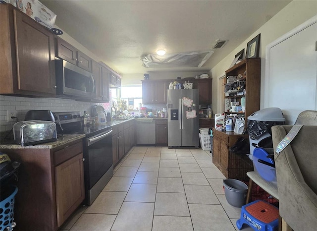 3074 NE Garden Ter, Palm Bay, FL 32905 - kitchen featuring appliances with stainless steel finishes, backsplash, light tile patterned floors, and dark stone counters