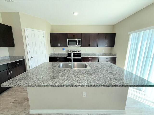 13118 Zolo Springs Cir, Riverview, FL 33579 - kitchen featuring stainless steel appliances, a sink, an island with sink, light stone countertops, and dark brown cabinetry