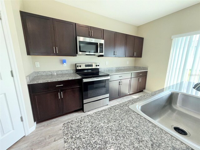 13118 Zolo Springs Cir, Riverview, FL 33579 - kitchen featuring appliances with stainless steel finishes, a sink, dark brown cabinets, light wood-type flooring, and light countertops