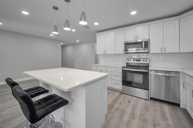 2307 N 47th St, Tampa, FL 33605 - kitchen with stainless steel appliances, a center island, light wood-style flooring, decorative backsplash, and a kitchen bar