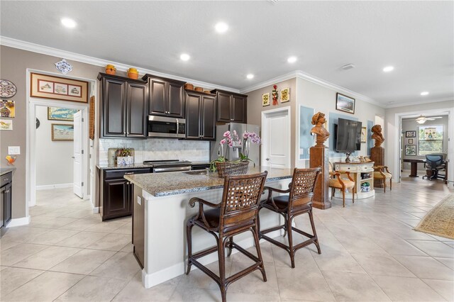 16898 Balance Cv, Land O Lakes, FL 34638 - kitchen with stainless steel appliances, decorative backsplash, ornamental molding, a kitchen bar, and a center island with sink