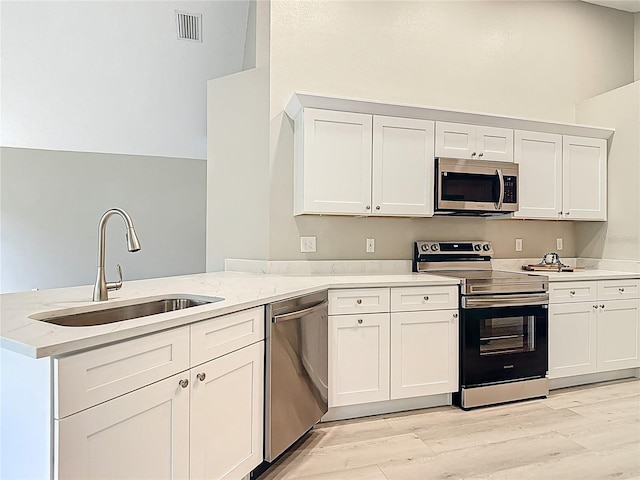 5809 Silas Creek Ln, Wesley Chapel, FL 33545 - kitchen with appliances with stainless steel finishes, a peninsula, white cabinetry, light wood-type flooring, and light stone counters