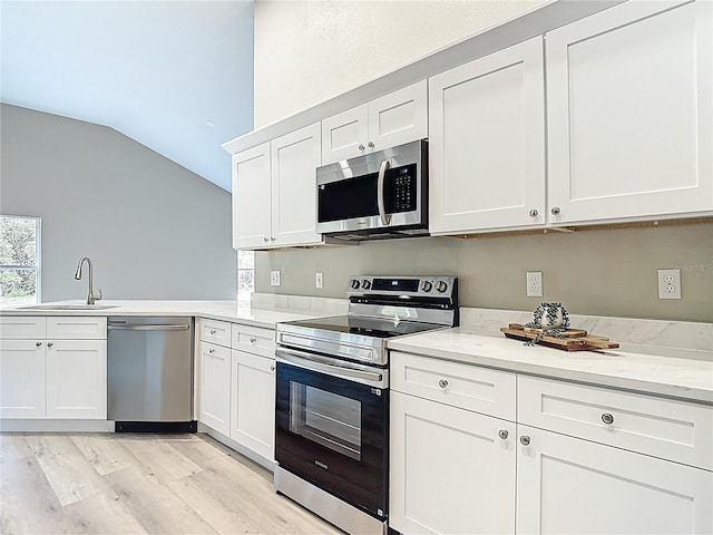 5809 Silas Creek Ln, Wesley Chapel, FL 33545 - kitchen featuring appliances with stainless steel finishes, lofted ceiling, light wood-style floors, white cabinets, and a peninsula