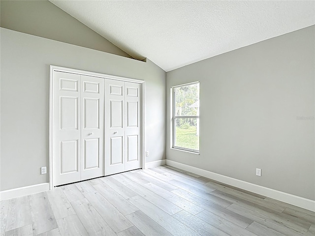 5809 Silas Creek Ln, Wesley Chapel, FL 33545 - unfurnished bedroom featuring light wood-style floors, lofted ceiling, a closet, and a textured ceiling