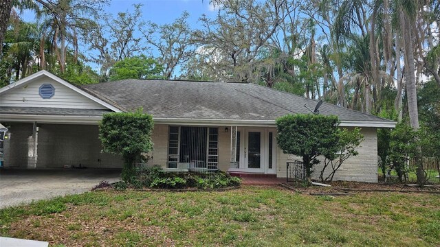 single story home featuring a front yard, roof with shingles, a porch, and a carport