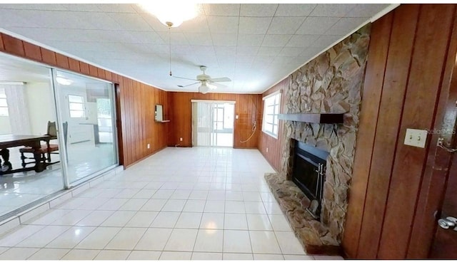 unfurnished living room featuring a ceiling fan, a fireplace, wooden walls, and light tile patterned floors