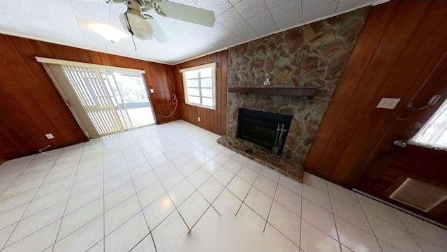 unfurnished living room featuring wooden walls, ceiling fan, a stone fireplace, and tile patterned flooring