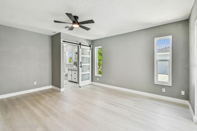 325 Gladstone Blvd, Englewood, FL 34223 - unfurnished bedroom with a barn door, light wood-style flooring, a textured ceiling, ensuite bath, and a ceiling fan