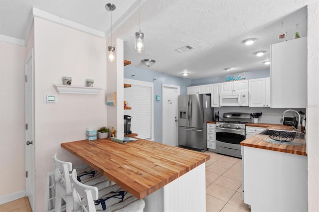 3905 31st Ave W, Bradenton, FL 34205 - kitchen with stainless steel appliances, wood counters, light tile patterned floors, a peninsula, and white cabinets