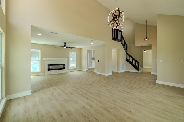 4044 Red Fox Ct, Wesley Chapel, FL 33543 - unfurnished living room featuring a high ceiling, light wood-style flooring, stairway, baseboards, and a glass covered fireplace