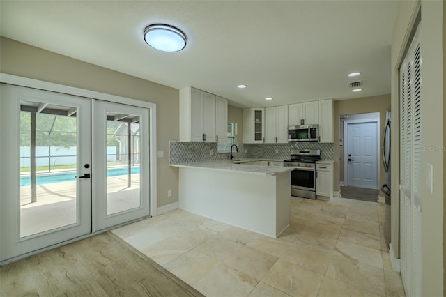4044 Red Fox Ct, Wesley Chapel, FL 33543 - kitchen with stainless steel appliances, a sink, a peninsula, french doors, and decorative backsplash