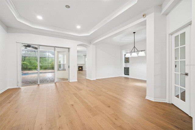 17802 Mission Oak Dr, Lithia, FL 33547 - unfurnished living room featuring a raised ceiling, light wood-style flooring, arched walkways, crown molding, and baseboards