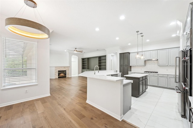 17802 Mission Oak Dr, Lithia, FL 33547 - kitchen with a center island with sink, a ceiling fan, gray cabinets, a glass covered fireplace, and cooktop