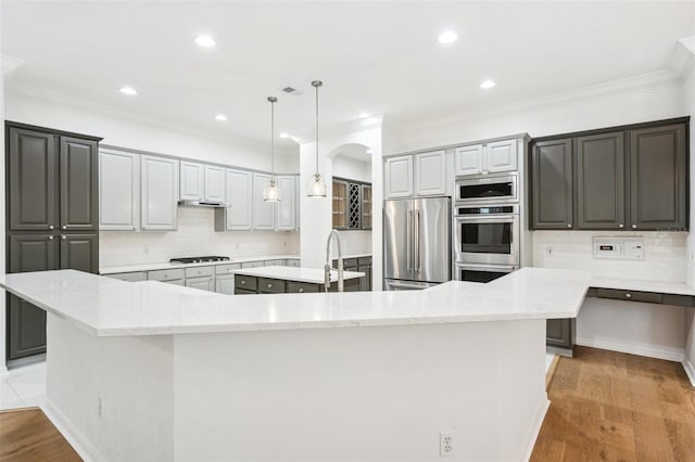 17802 Mission Oak Dr, Lithia, FL 33547 - kitchen featuring appliances with stainless steel finishes, a large island with sink, arched walkways, backsplash, and crown molding