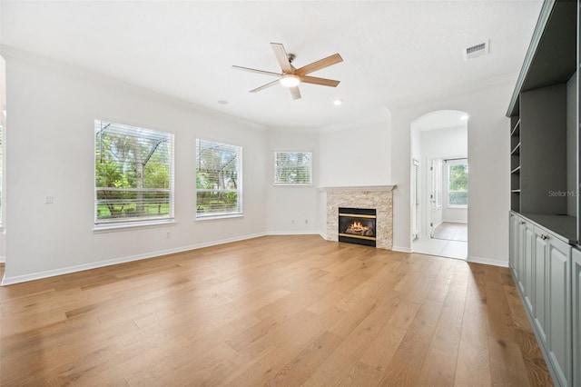 17802 Mission Oak Dr, Lithia, FL 33547 - unfurnished living room with a ceiling fan, crown molding, light wood-style flooring, arched walkways, and a stone fireplace