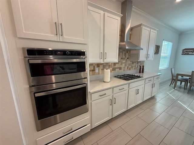 17304 Scuba Crest St, Wimauma, FL 33598 - kitchen featuring wall chimney exhaust hood, double oven, crown molding, tasteful backsplash, and white cabinets
