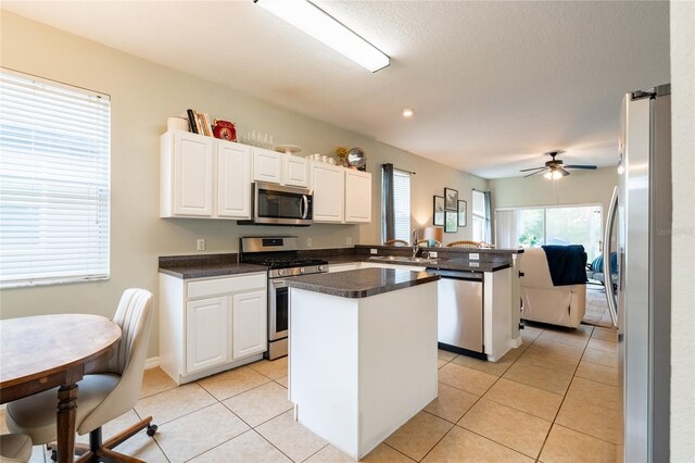 14320 Tree Swallow Way, Lakewood Ranch, FL 34202 - kitchen featuring appliances with stainless steel finishes, a center island, a peninsula, dark countertops, and white cabinetry