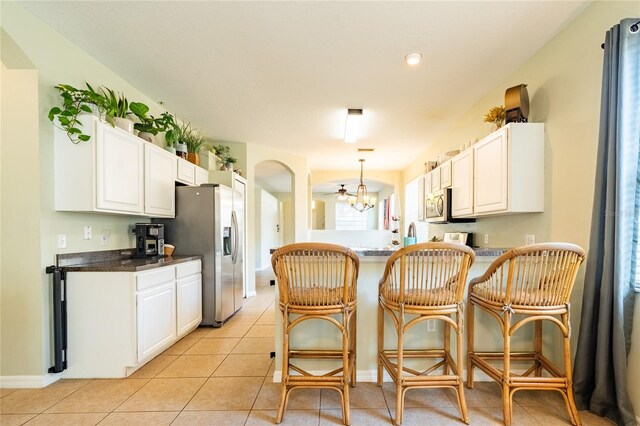 14320 Tree Swallow Way, Lakewood Ranch, FL 34202 - kitchen with stainless steel appliances, dark countertops, a peninsula, a chandelier, and white cabinets