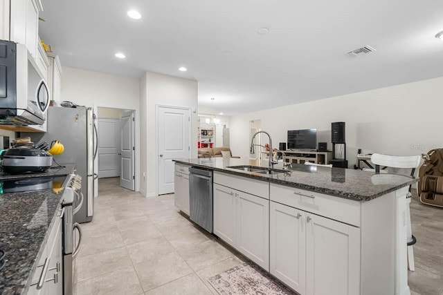 5006 Jackel Chase Dr, Wimauma, FL 33598 - kitchen featuring appliances with stainless steel finishes, a sink, dark stone countertops, an island with sink, and white cabinets