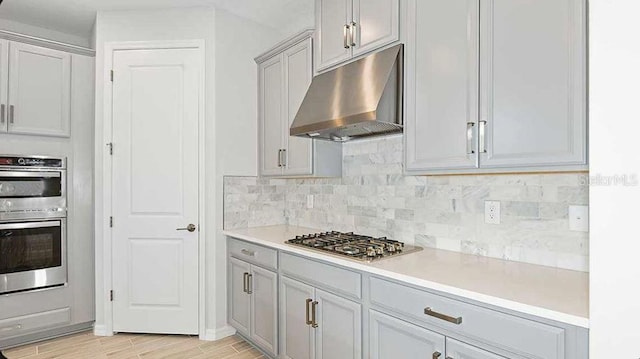 33306 Castaway Loop, Wesley Chapel, FL 33543 - kitchen featuring under cabinet range hood, appliances with stainless steel finishes, backsplash, light countertops, and light wood-style floors