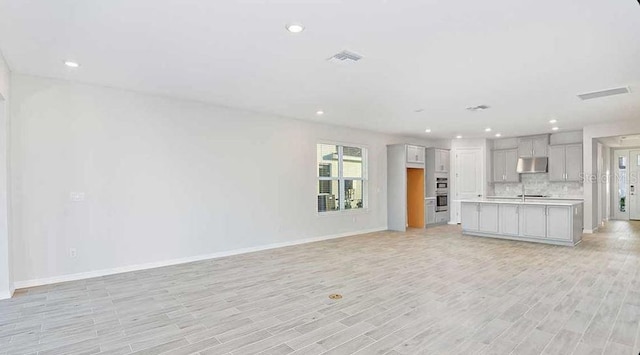 33306 Castaway Loop, Wesley Chapel, FL 33543 - unfurnished living room featuring recessed lighting, baseboards, a sink, and light wood-style flooring