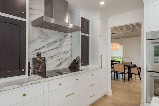 2395 Campbell Rd, Clearwater, FL 33765 - kitchen featuring wall chimney range hood, light wood-type flooring, white cabinetry, and black electric cooktop
