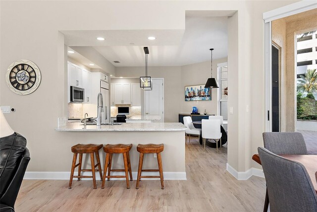 100 Beach Dr NE Unit 301, Saint Petersburg, FL 33701 - kitchen with appliances with stainless steel finishes, a peninsula, light wood-style floors, white cabinetry, and baseboards