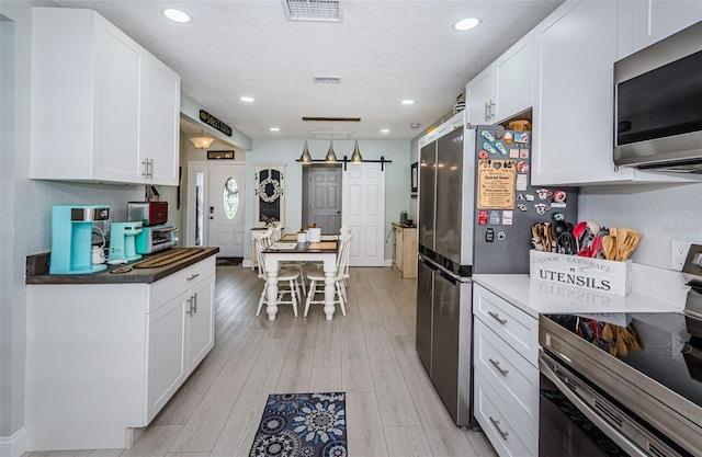 7547 Landmark Dr, Spring Hill, FL 34606 - kitchen with appliances with stainless steel finishes, white cabinets, a barn door, recessed lighting, and a textured ceiling