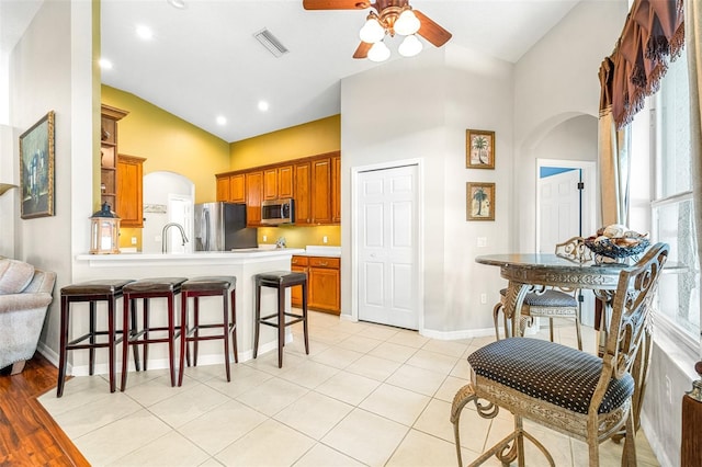 8814 N River Rd, Tampa, FL 33635 - kitchen with appliances with stainless steel finishes, a ceiling fan, brown cabinets, a breakfast bar, and a peninsula