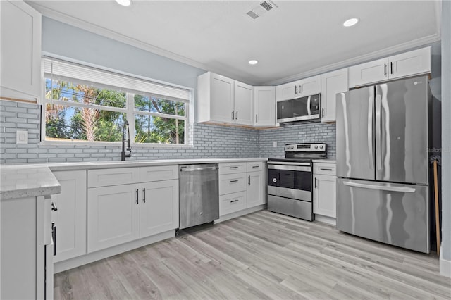 4841 Drift Tide Dr, New Port Richey, FL 34652 - kitchen with stainless steel appliances, crown molding, backsplash, white cabinets, and light wood-type flooring