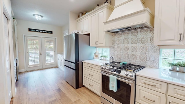 9800 Sago Point Dr, Seminole, FL 33777 - kitchen featuring premium range hood, stainless steel appliances, light wood-style floors, backsplash, and french doors