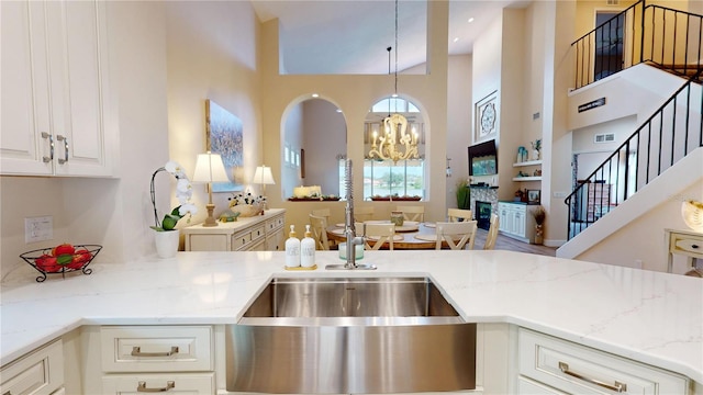 9800 Sago Point Dr, Seminole, FL 33777 - kitchen with a high ceiling, light stone countertops, a chandelier, white cabinets, and a sink