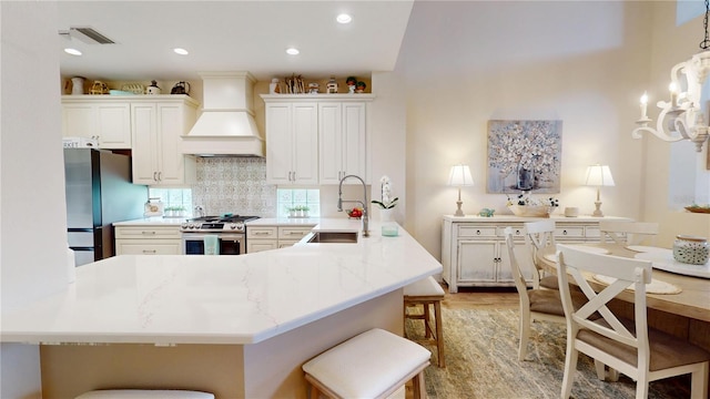 9800 Sago Point Dr, Seminole, FL 33777 - kitchen featuring stainless steel appliances, premium range hood, a breakfast bar, tasteful backsplash, and white cabinetry