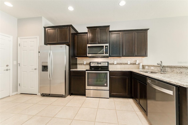 9140 Hillcroft Dr, Riverview, FL 33578 - kitchen featuring appliances with stainless steel finishes, a sink, dark brown cabinetry, decorative backsplash, and light stone counters