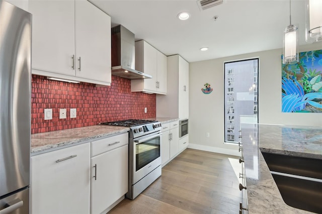 199 Dali Blvd Unit 607, Saint Petersburg, FL 33701 - kitchen with wall chimney exhaust hood, appliances with stainless steel finishes, light wood-style flooring, backsplash, and white cabinets